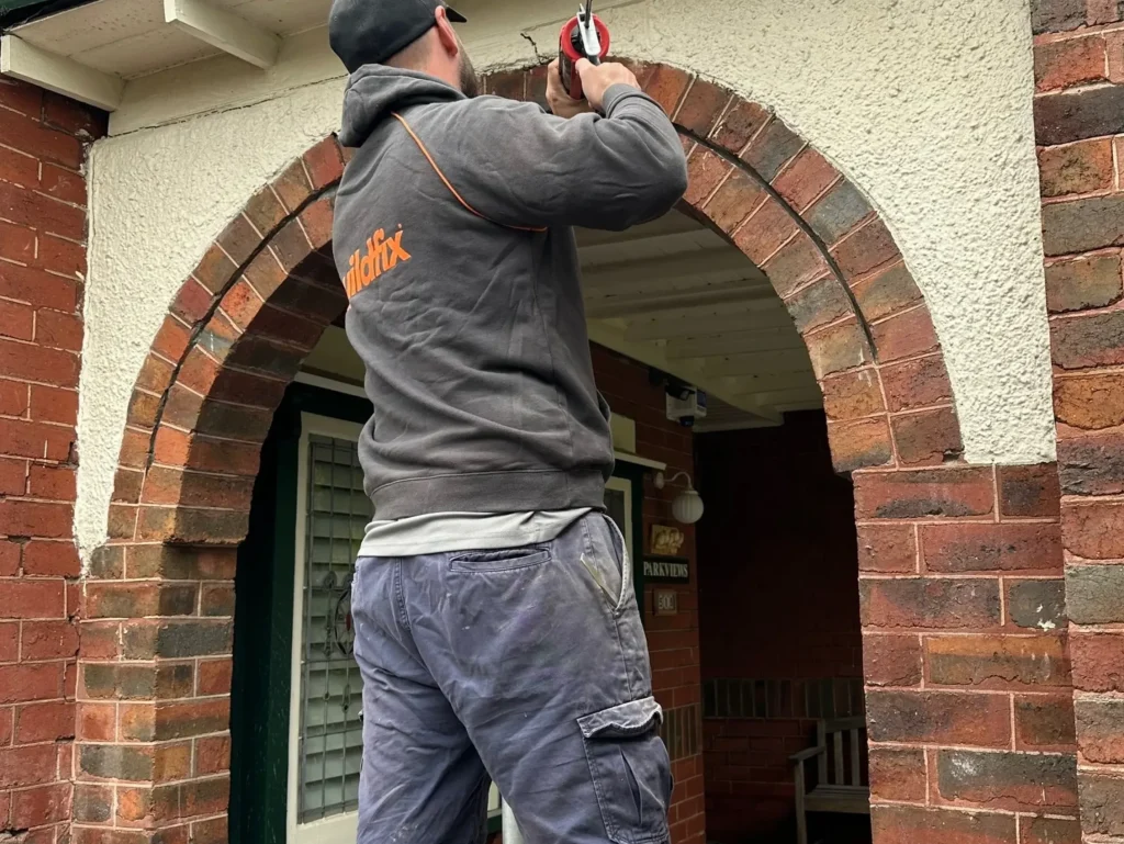 Technician installing security camera above brick archway to monitor wall cracks.